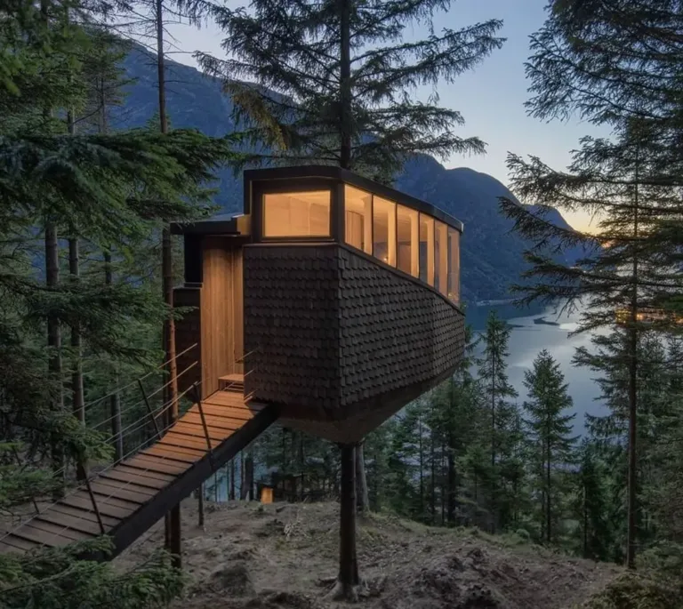 Woodnest treehouse in Norway, a shingle-clad cabin on stilts offering panoramic fjord views through its band of windows—a Scandinavian-inspired treetop retreat.