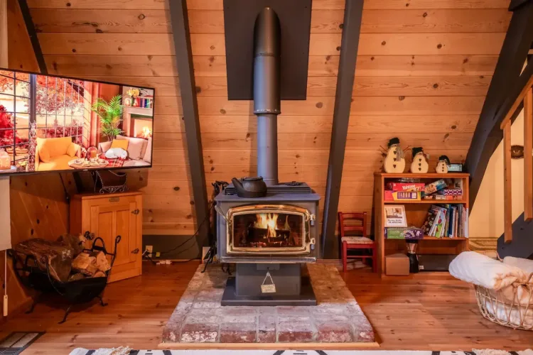 Close-up of a Pacific Energy wood burning stove in a rustic simple A-frame house interior with wood paneling.