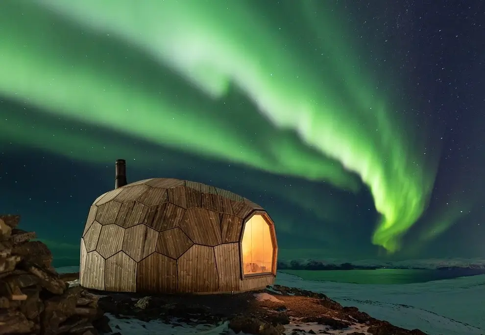Stunning Hammerfest Hiking Cabin in Norway, a domed wooden structure glowing under the Northern Lights, showcasing Nordic shelter design.