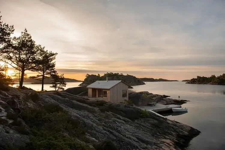 Cozy Norwegian cabin exterior clad in warm pine, blending seamlessly with the rocky coastline and offering sea views.
