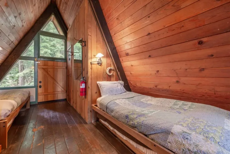 Rustic interior of a tiny A-frame cabin ('Irwin A-Frame') with two simple beds and wood-paneled walls.
