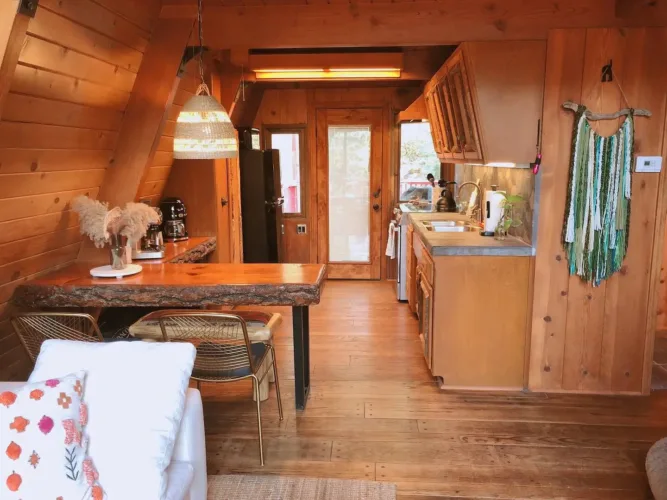 Cozy simple A-frame house interior of 'Shasta' tiny cottage with a live-edge table and bohemian decor.