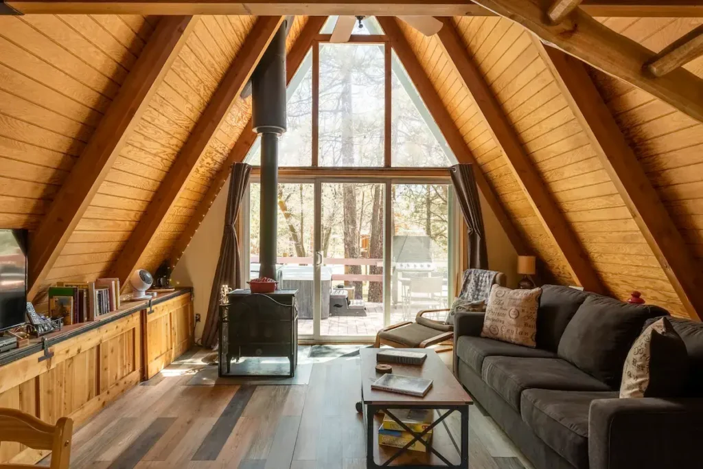 Bright and airy classic A-frame cabin interior with light wood, wood stove, and large window opening to a deck.
