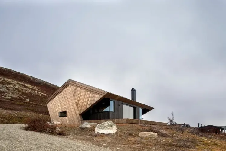 The Hooded Cabin in Norway, a modern mountain dwelling with a distinctive angular roof and mixed wood cladding, showcasing Scandinavian design adapted for rugged landscapes.