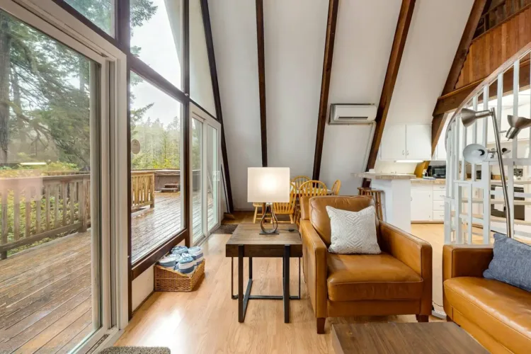 Contemporary simple A-frame house interior with white walls, tan leather furniture, spiral staircase, and deck view.