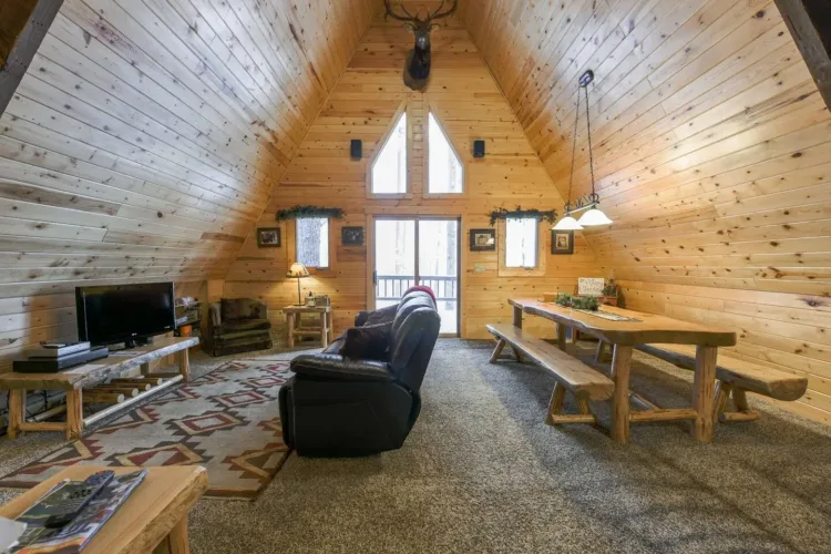 Spacious rustic A-frame cabin interior ('Cozy Bear Cabin') with light wood paneling and taxidermy accent.