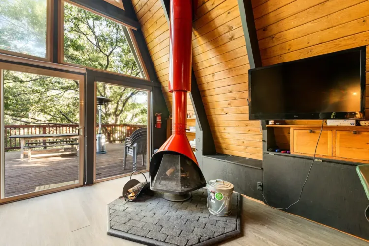 Modern A-frame cabin ('moderne finnhütte') interior highlighting a vibrant red retro freestanding fireplace.