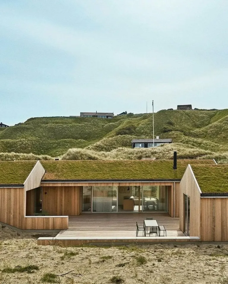 Danish summer cabin exterior with warm cedar siding and a grassy roof, designed to blend with the natural landscape.