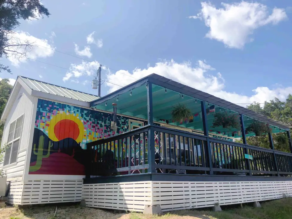 Design of 'Wild & Free Tinyhome Glamping' near Garner Park, TX, showcasing a colorful mural, covered porch, and a spectacular starry night sky ideal for stargazing.