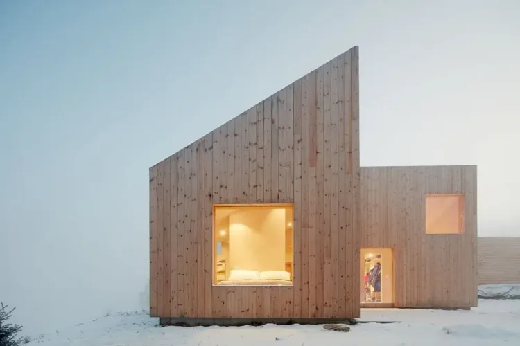 Cozy Norwegian cabin in a pine forest with a multi-gabled roof and untreated pine exterior, designed for snowy climates.