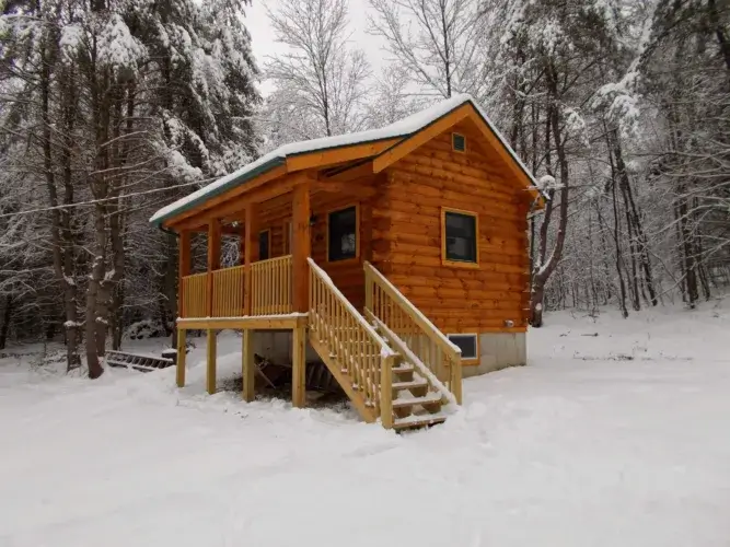 The Backwoods log cabin kit nestled in a snowy, wooded setting, perfect for a winter retreat.