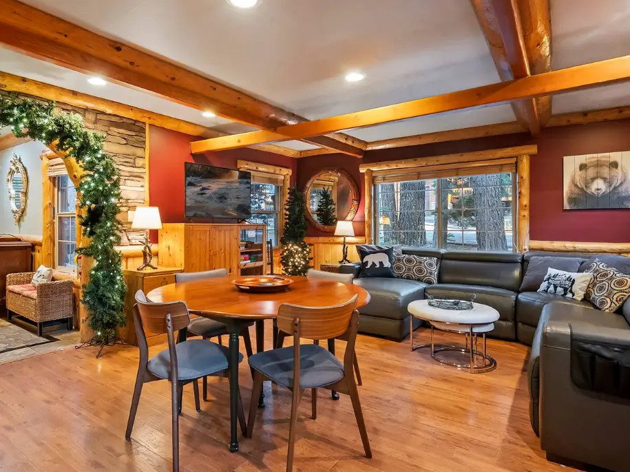 The cozy great room of a Big Bear log cabin, featuring a large leather sofa and a dining area under exposed wood beams.