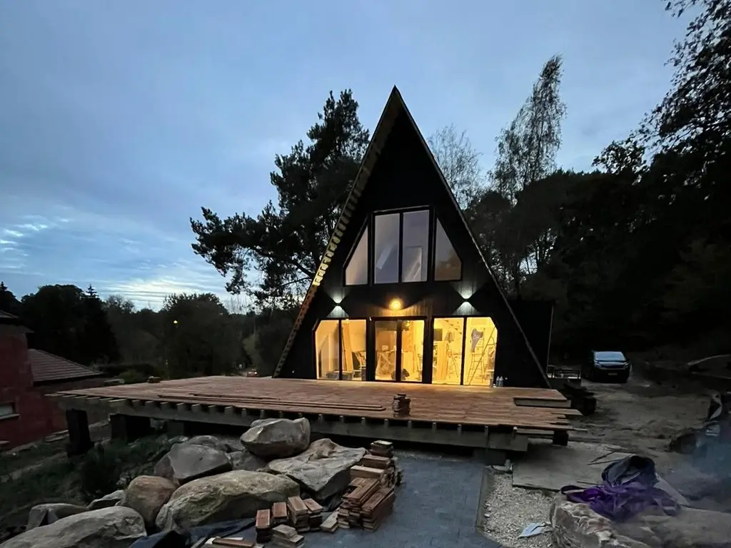 Sleek, modern Scandinavian A-frame house at dusk, showcasing large floor-to-ceiling windows and warm interior lighting.