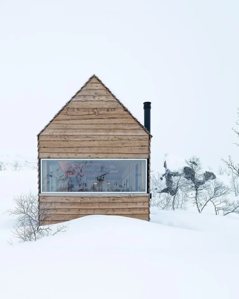 Long, narrow off-grid cabin perched on a Norwegian hillside, featuring a natural wood exterior and large windows.
