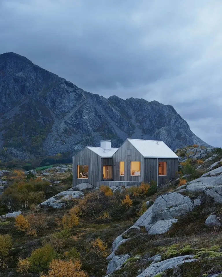 Modern Scandinavian cottage exterior on a Norwegian island, featuring large windows and blending with granite cliffs.