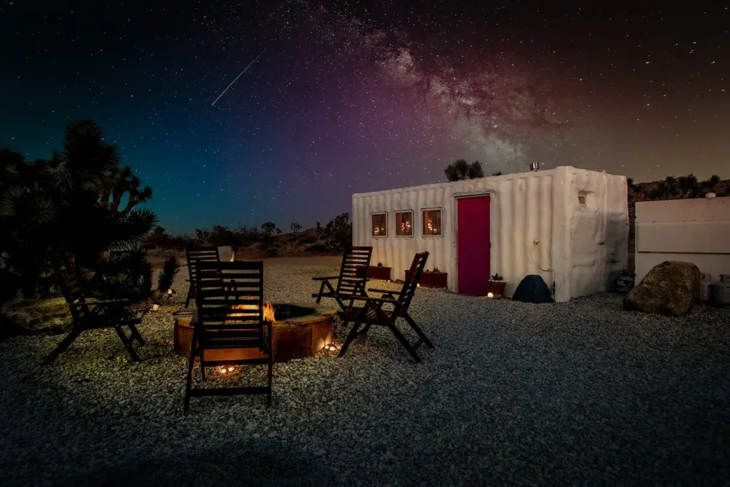 Design of Moon Camp, a Joshua Tree shipping container home, featuring a white exterior, red door, and a cozy fire pit perfectly situated for enjoying the Milky Way and desert night sky.