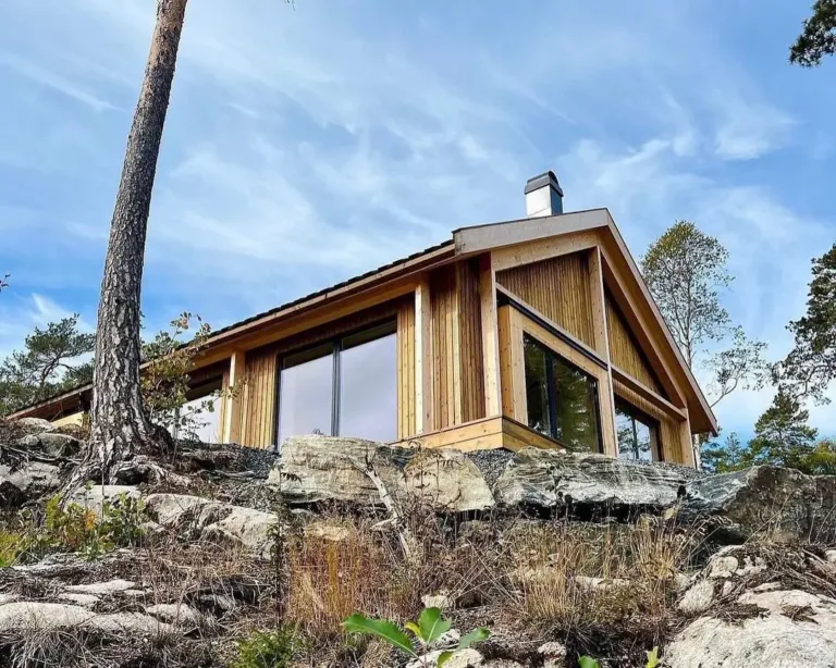 Modern Norwegian cabin exterior with solid wood construction and large bay windows, blending tradition with contemporary style.