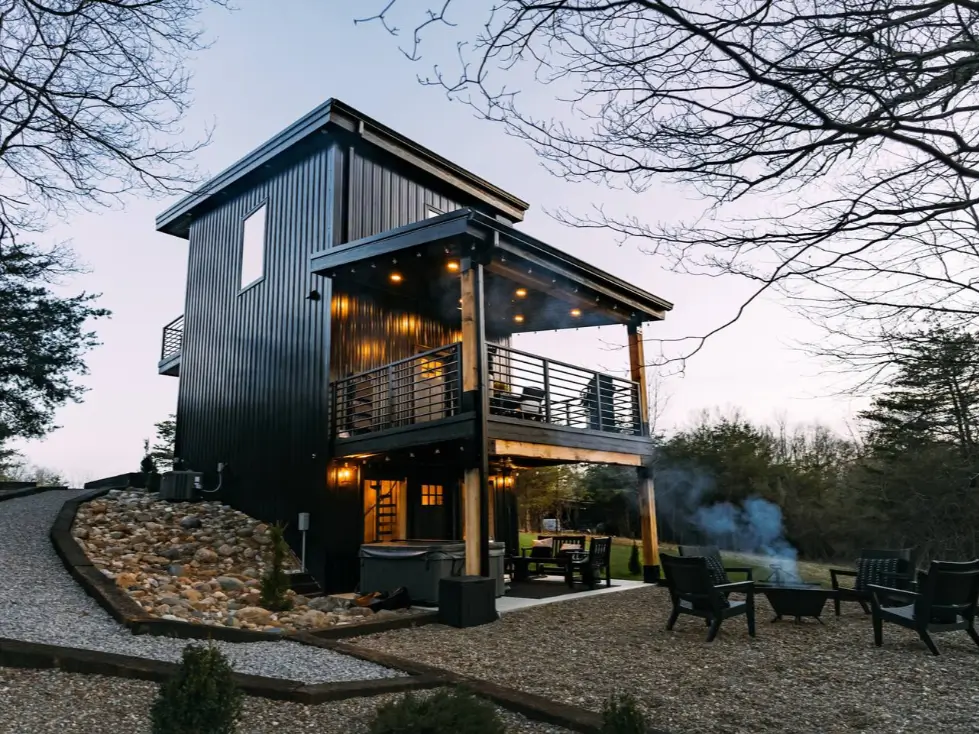 Parker's Point, a modern three-story black shipping container home design in Logan, OH, showcasing a tall, narrow vertical architecture with a balcony in a woodland clearing.