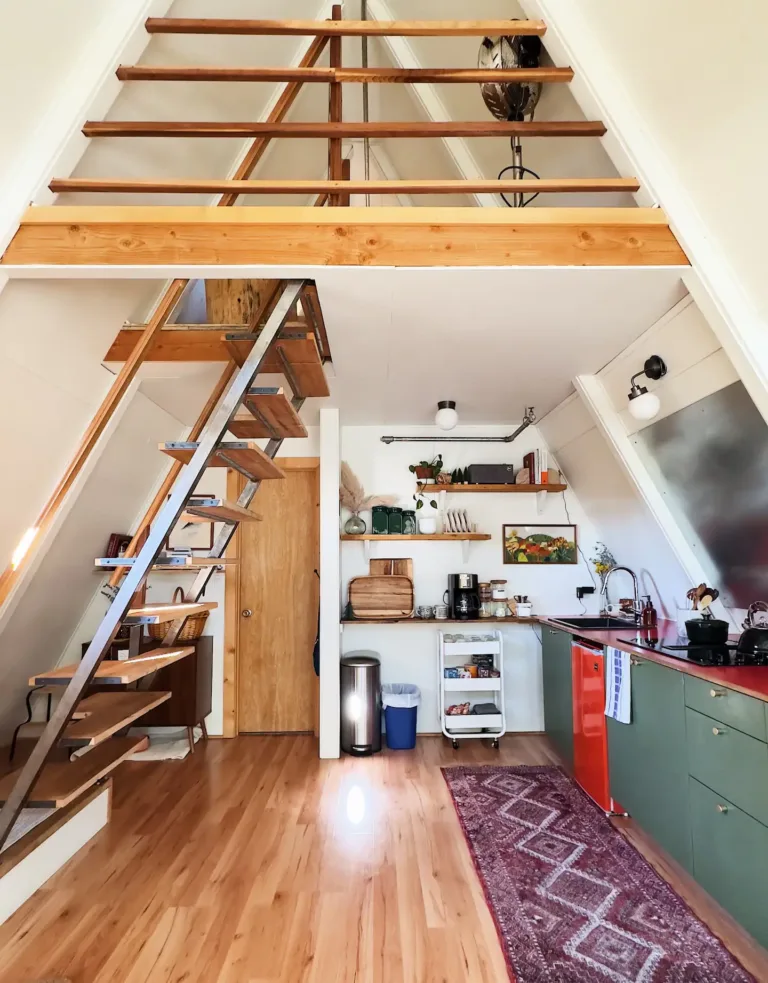 Bright A-frame house interior kitchen in 'The Winnie' with green cabinets, red accents, and ladder to loft.