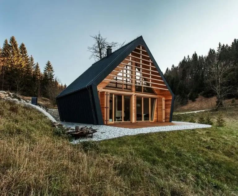Modern wooden house exterior in Slovenia with extensive glass walls, designed to integrate with the surrounding forest.