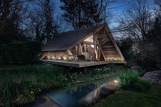 Cozy wooden cabin exterior with a large deck, situated by woods and a stream, ideal for a guest retreat.