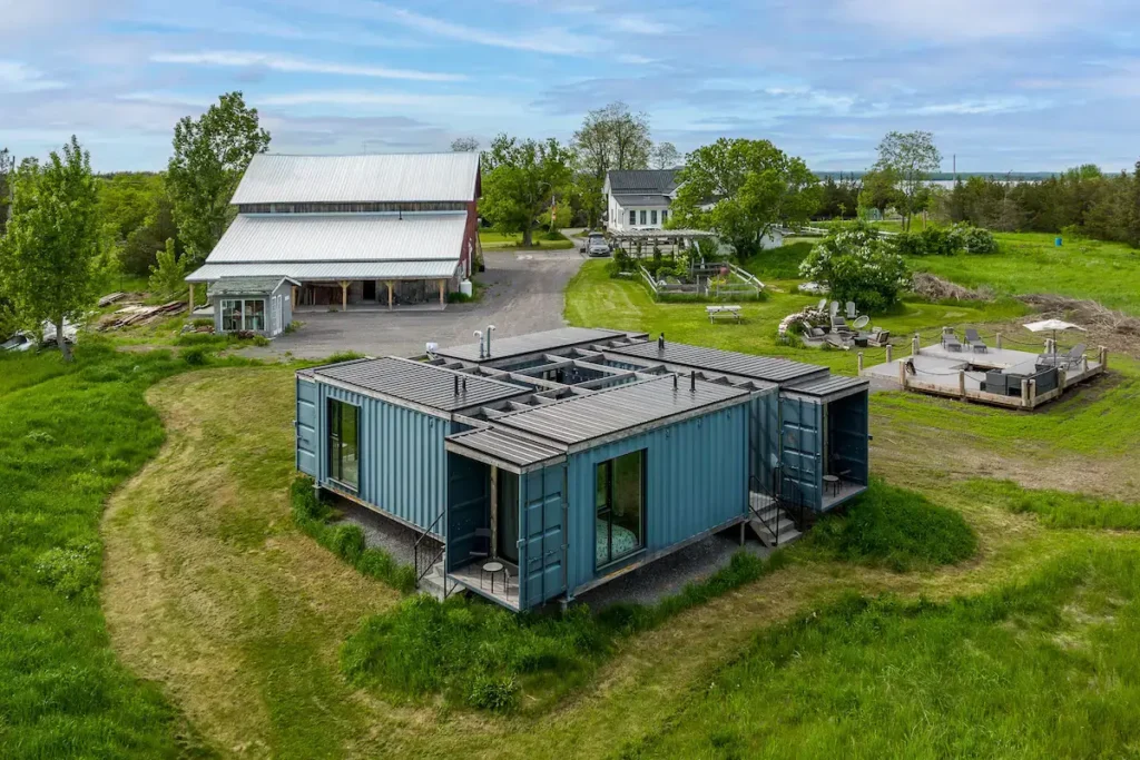 Unique shipping container home design of The Acres at High Shore in Prince Edward County, Canada, showcasing a pinwheel layout of blue-grey containers forming a central courtyard.