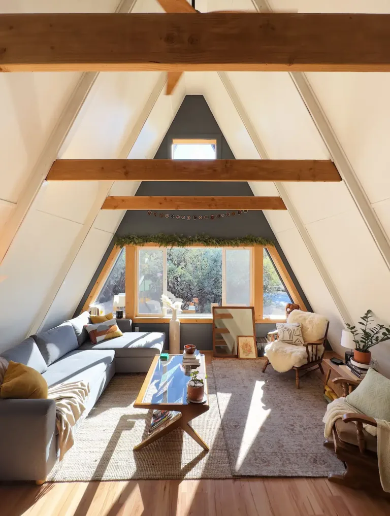 Sun-drenched simple A-frame house interior living room in 'The Winnie' with large gable window and modern-cozy decor.