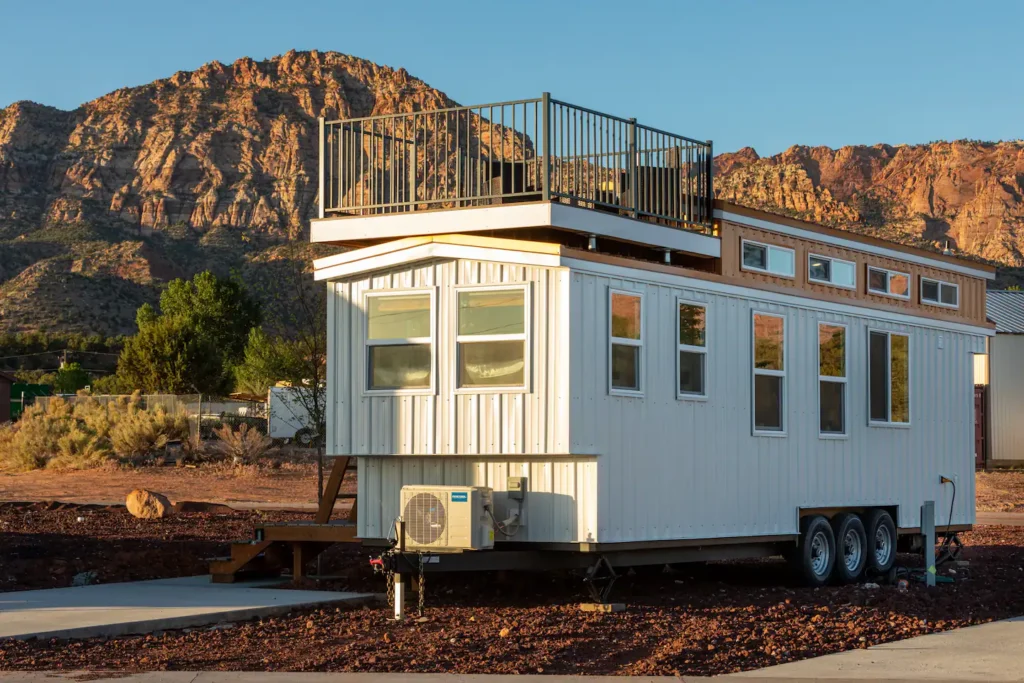 Aloha Tiny Home design in Apple Valley, UT, a white mobile shipping container-style tiny home with a rooftop deck for panoramic views of desert mountains.