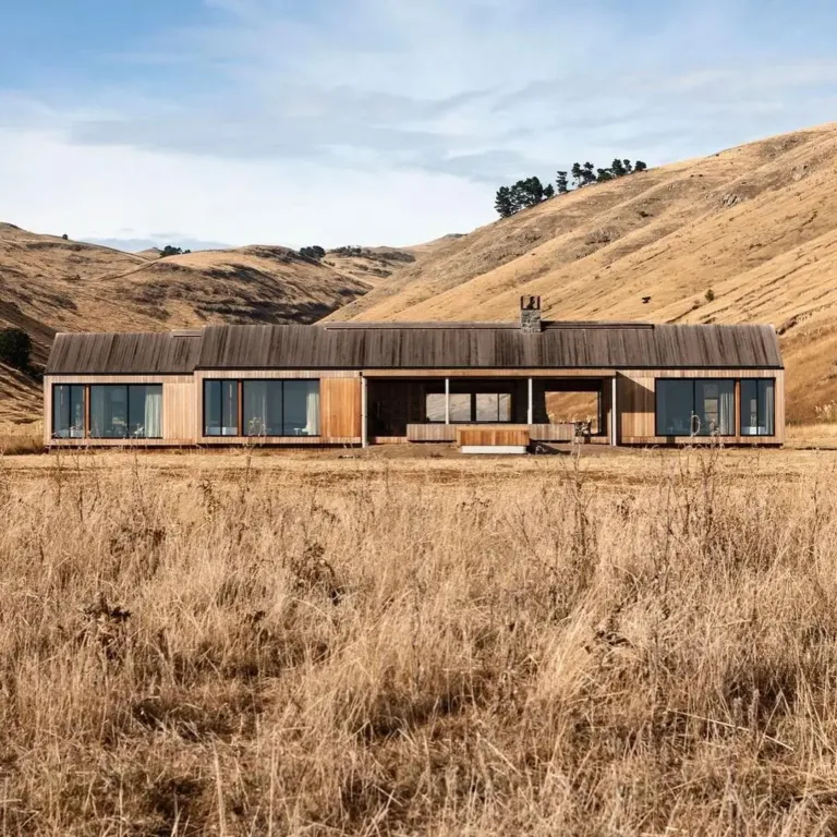 Resilient New Zealand farmhouse exterior with natural stone and wood, designed to withstand coastal storms.