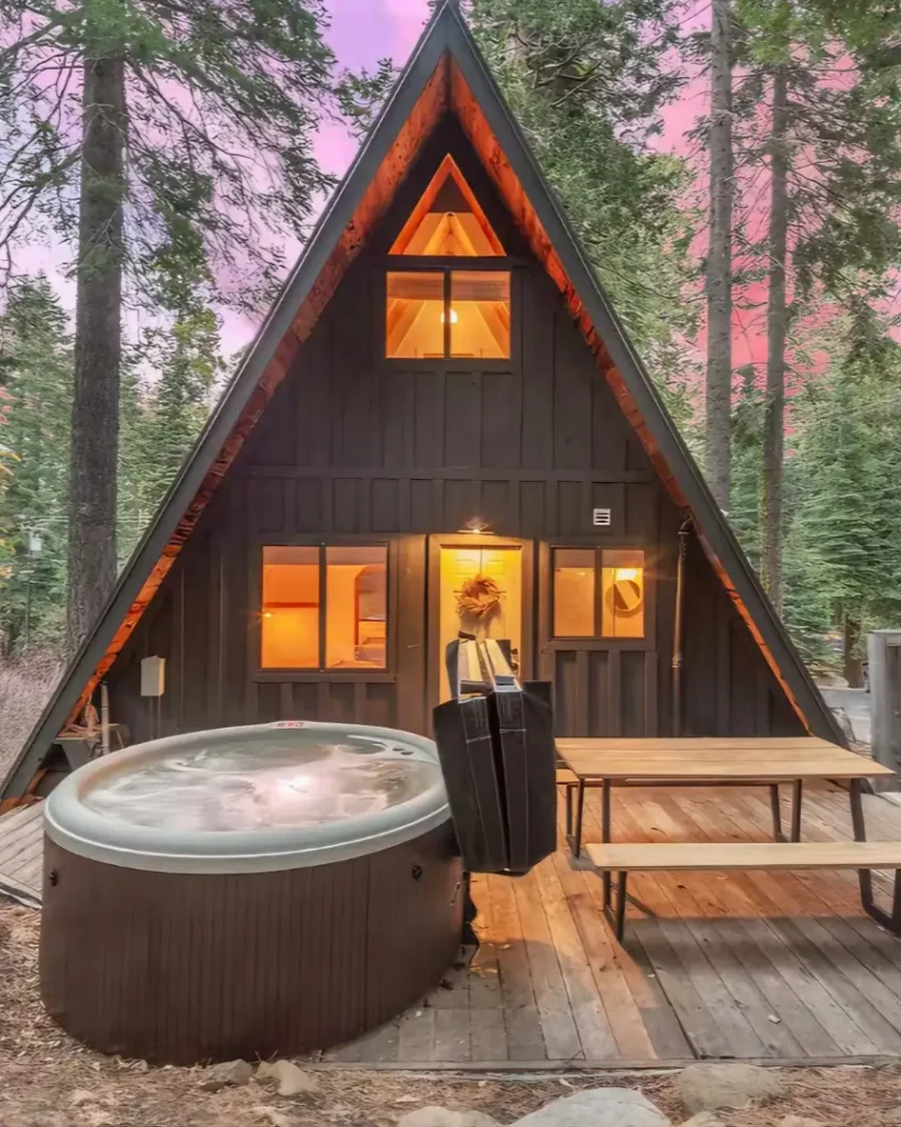 A-Frame-Prime, a classic Tahoe A-frame cabin on the West Shore, shown at twilight with its inviting deck, hot tub, and surrounding forest.