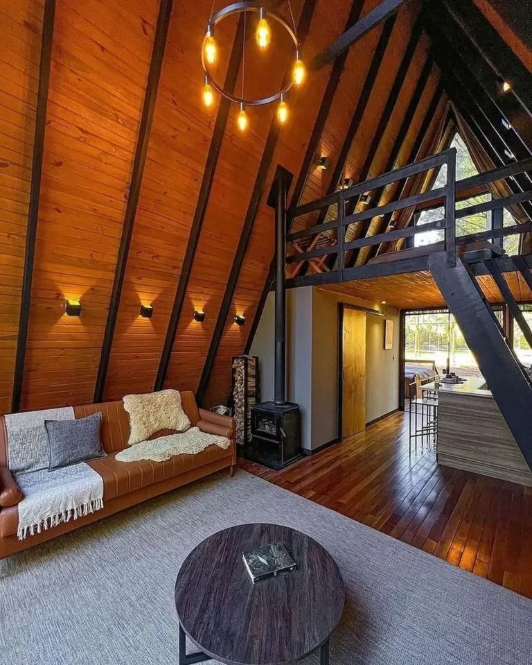 Warm, orange-toned all-wood A-frame house interior of 'Cabana Alameda' with dark beams and wood stove.