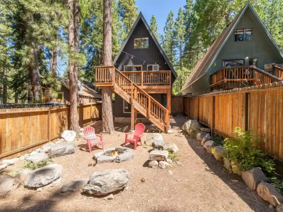 The private, fenced-in backyard of the #BrookAframe cabin in Kings Beach, featuring a fire pit area with red chairs, perfect for a cozy Tahoe A-frame getaway on the North Shore.