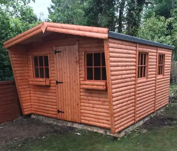 A large, premium shed log cabin with a side storage unit and double glass doors, installed on a clean wooden deck foundation.