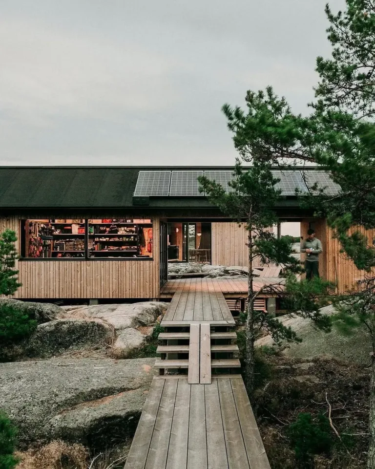 Sustainable Finnish house exterior with natural wood siding and a solar panel on the roof, blending with the rocky landscape.