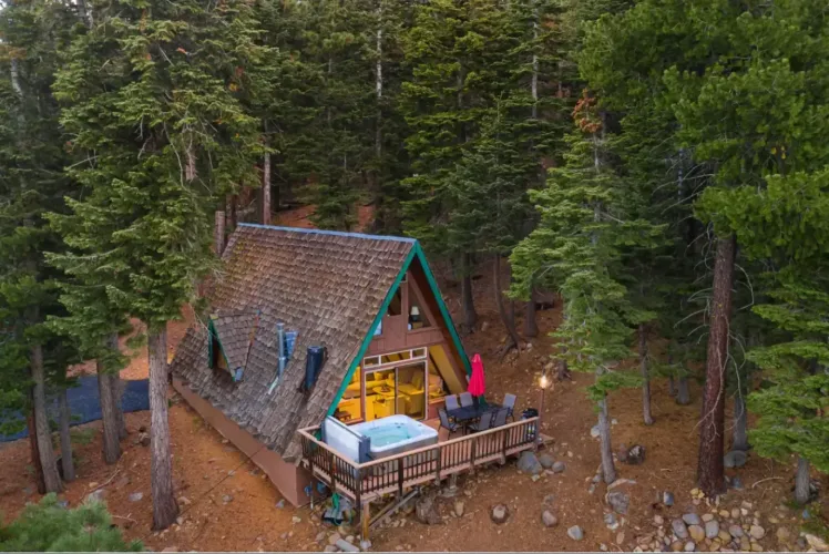 An aerial view of the Adorable Lakeview A-frame cabin in Tahoe City, a cozy retreat with a hot tub on the deck, nestled among tall pine trees on the North Shore.