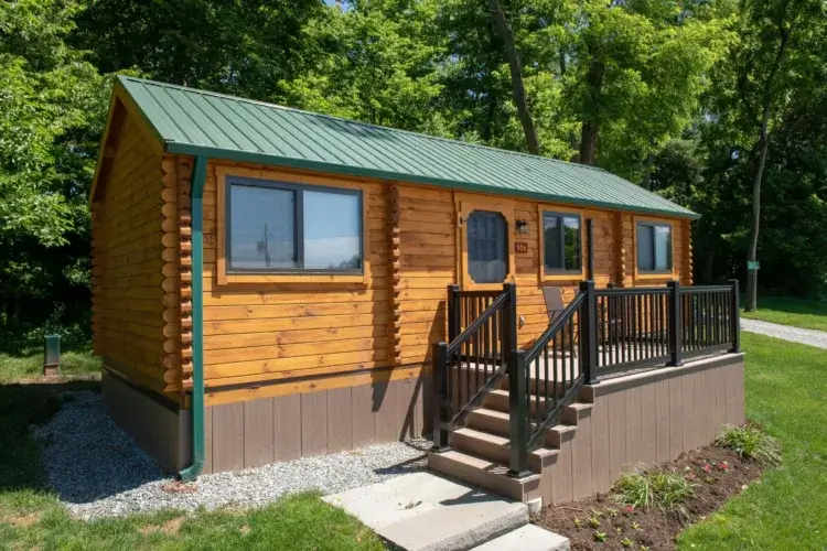 The Rancher-style small log cabin kit with a dark railing set in a landscaped yard.