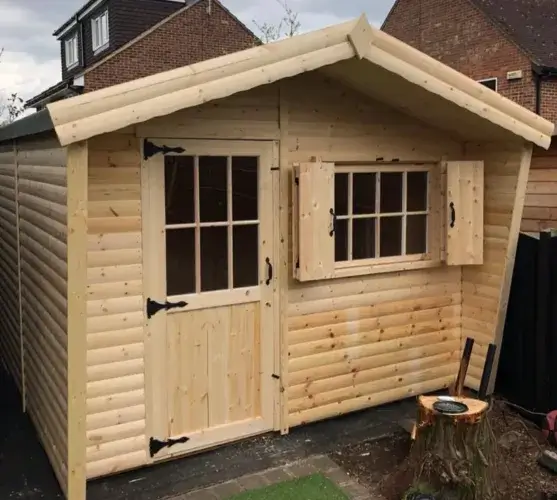 A well-maintained, compact shed log cabin with a modern pent roof, sitting on a flagstone patio with a small dog in front.