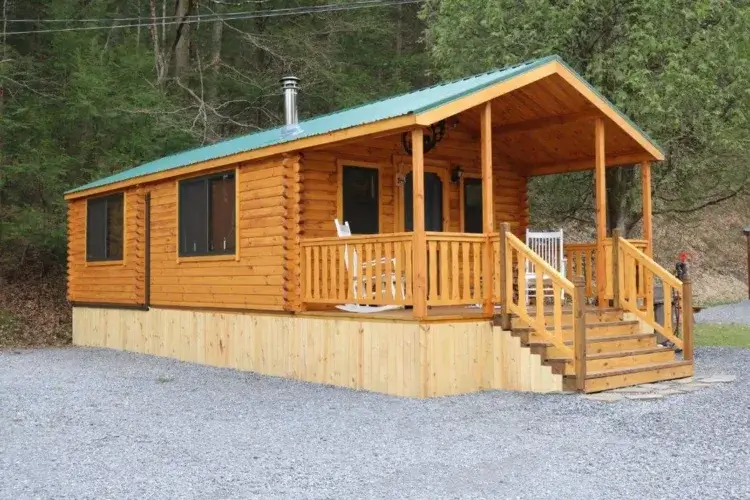 The Adirondack log cabin kit featuring a large covered porch and a chimney for a wood stove.