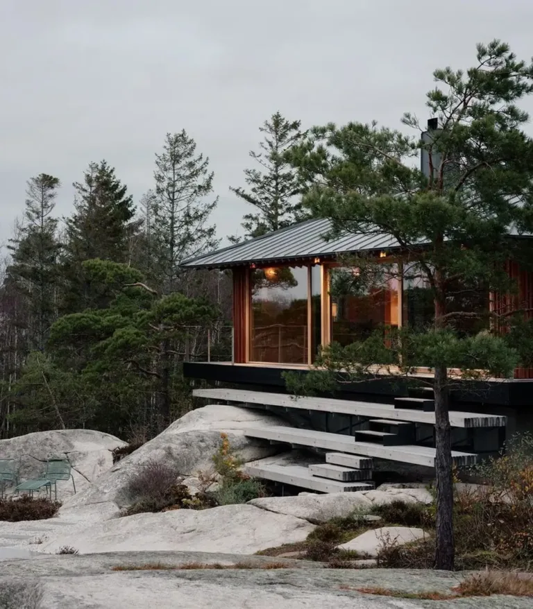 Contemporary Norwegian cabin exterior with a wide deck, natural wood, and large windows overlooking a scenic view.