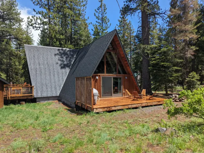 The Dazzling Chalet, a classic Tahoe A-frame on the West Shore, with a spacious wooden deck and surrounded by a grassy meadow and tall pine trees.