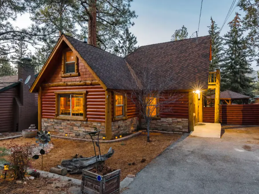 The inviting exterior of a classic Big Bear log cabin rental at twilight, with warm lights glowing from the windows.