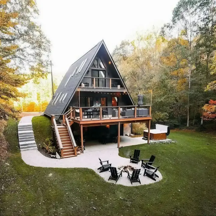 Modern A-frame house with a dark exterior, featuring expansive multi-level decks with outdoor furniture, a fire pit area, and hot tub, showcasing impressive outdoor living design for A-frames.