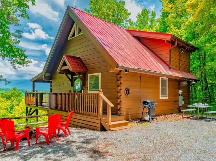Rustic log cabin in Gatlinburg with red roof, spacious deck, outdoor seating, and mountain views.