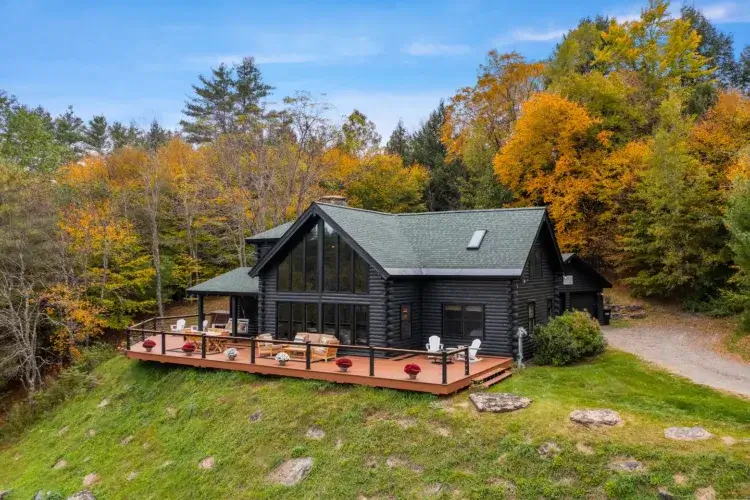 A stunning log cabin rental in Vermont with a large deck overlooking a hillside with vibrant fall foliage.