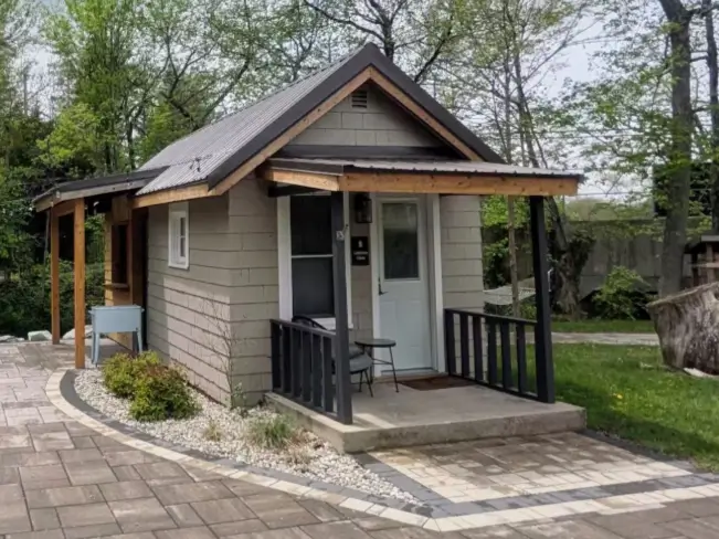 A charming tiny house on a permanent foundation in Ohio, featuring a covered porch and metal roof.
