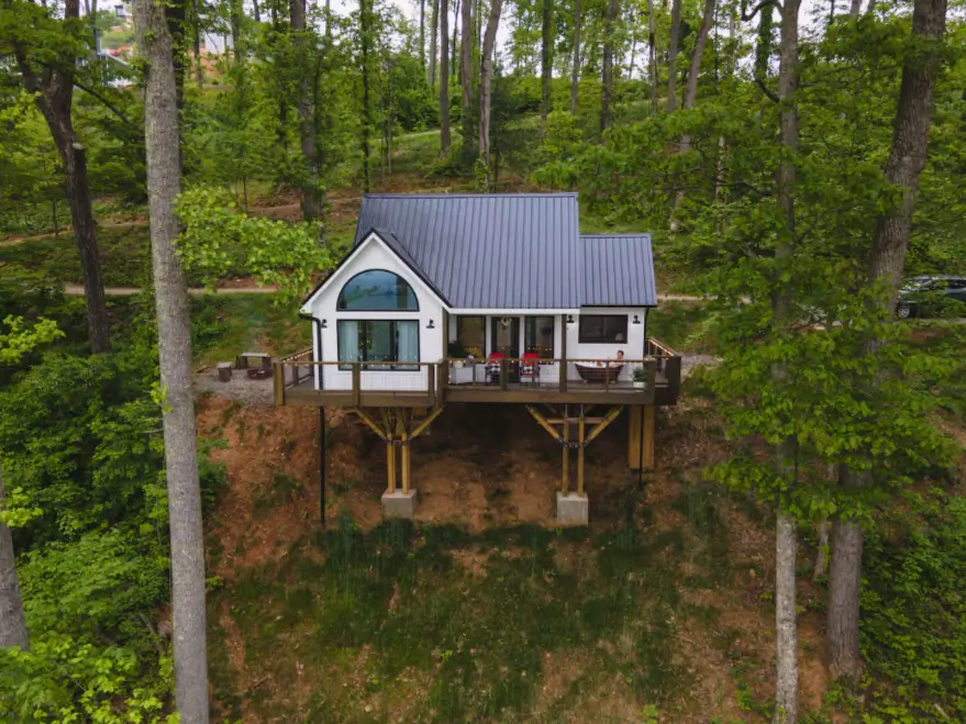 The exterior of the modern farmhouse treehouse in Asheville, NC, nestled on a wooded hillside with its expansive deck visible.