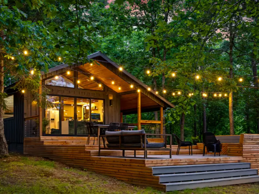 The exterior of The Coalmont cabin at dusk, with warm string lights illuminating the modern wooden deck and surrounding Tennessee forest.