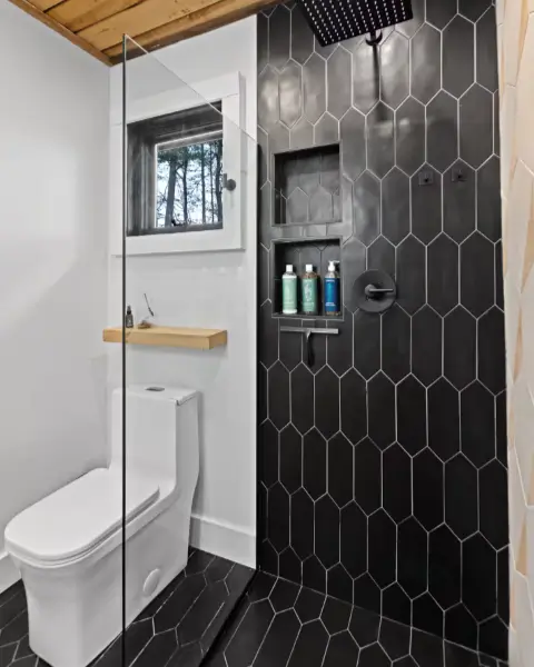 The modern bathroom at The Coalmont cabin, with a stylish black-tiled walk-in rain shower and a window view of the forest.