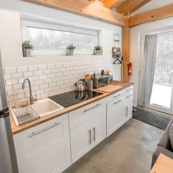 The efficient tiny house kitchen layout in the Honeycrisp Cottage, featuring a long countertop with an induction cooktop, butcher block counters, and a white subway tile backsplash.