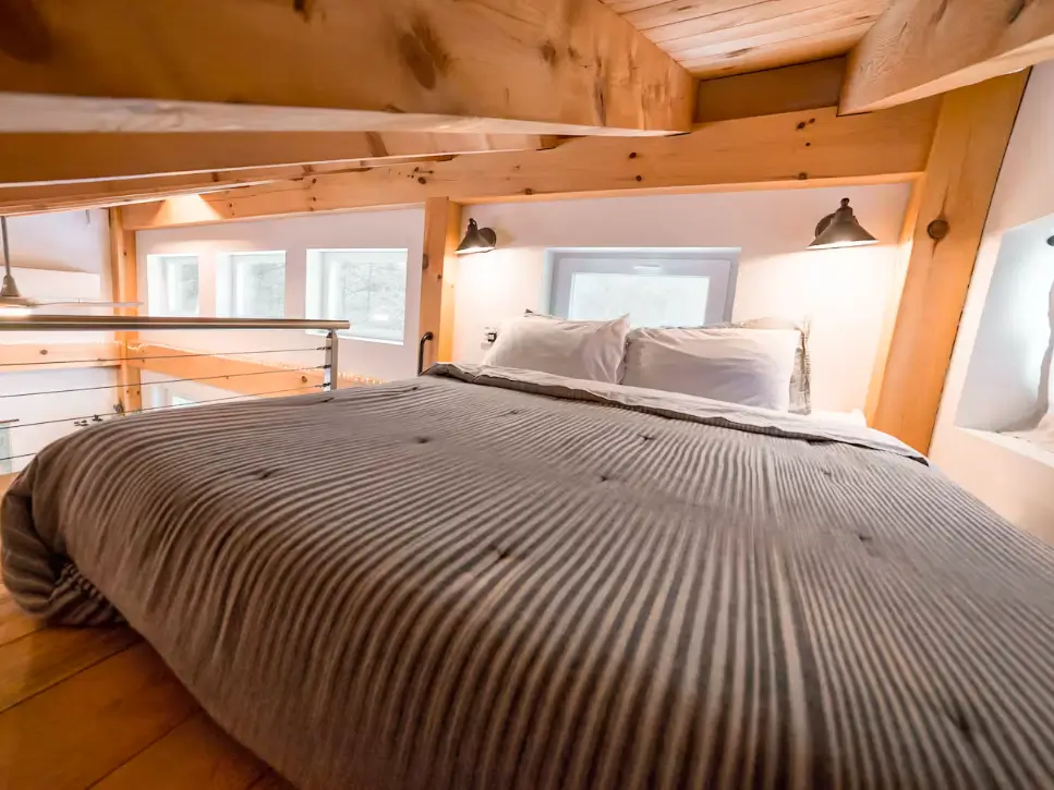 The cozy sleeping loft in the 2 bedroom tiny house, featuring a comfortable bed nestled under the exposed wood beams of the ceiling.